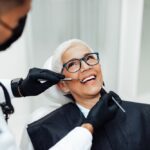 A woman having her veneers examined by a dentist. She is sitting back in the dentist's chair and smiling.